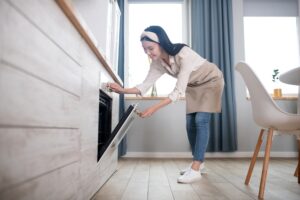 Young woman in a head bandage opening the oven door.